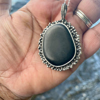 Black Beach Stone in my hand showing side view. Black Beach Stone in Water Background. Bohemian necklace Bold necklace Beautiful necklace Sterling silver necklace Goddess necklace Sexy necklace Textured necklace Statement necklace Unique necklace  Cosmic necklace