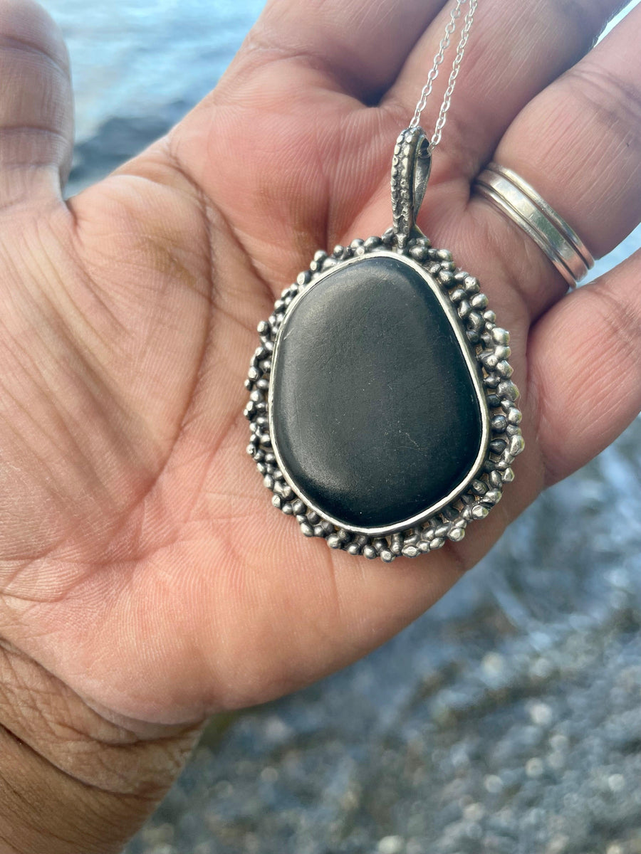 Black Beach Stone in my hand showing side view. Black Beach Stone in Water Background. Bohemian necklace Bold necklace Beautiful necklace Sterling silver necklace Goddess necklace Sexy necklace Textured necklace Statement necklace Unique necklace  Cosmic necklace